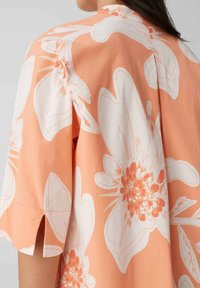 Perzik bloes met witte grote bloemprint, korte mouwen met uitsneden, lichtgewicht stof en een ontspannen pasvorm.