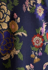 Granatowy materiał z dużymi wzorami kwiatowymi w odcieniach purpury, czerwieni, żółci i różu, przetykany zielonymi liśćmi, o teksturowanym i żywym designie.