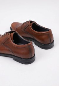 Zapatos de cuero marrón con una textura suave, diseño de cordones y suela de goma negra. Presentan costuras sutiles y una forma de punta redondeada.