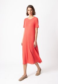 Korallinvärinen, polvipituinen mekko, jossa on ribbitoitu pinta ja lyhyet hihat. Mekossa on pyöreä kaula-aukko ja se laskeutuu väljästi, yhdessä tasapohjaisten kenkien kanssa.