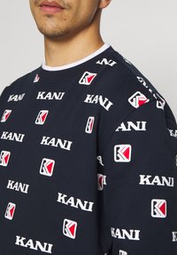Felpa blu navy in cotone, con loghi bianchi e rossi "KANI" sparsi in riquadri e colletto bianco a costine.