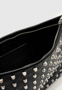 Czarna skórzana torebka z srebrnymi ćwiekami w kształcie piramid, zamkiem błyskawicznym oraz podszytym wnętrzem, w którym widać czarny etui na karty i detale zamka.