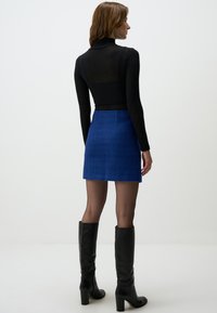 Haut noir ajusté à col roulé associé à une mini-jupe bleue texturée. Des bottes noires à talon haut arrivant jusqu'aux genoux complètent la tenue.