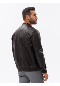 Giubbotto bomber in pelle marrone con polsini e orlo a costine, presenta una texture liscia, una tasca con zip sulla manica e un design classico del colletto.