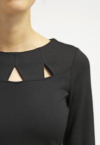 Czarny długi rękaw top z okrągłym dekoltem oraz trzema trójkątnymi wycięciami na klatce piersiowej, wykonany z elastycznej tkaniny o teksturowanym wyglądzie.