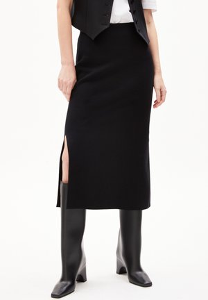 Sort strikket midi-nederdel med sideslip, tekstureret stof og en tætsiddende pasform, kombineret med knælange sorte støvler.