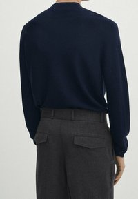 Laivastonsininen villapaita pitkine hihoineen, sileä pintakuosi ja minimalistinen muotoilu, yhdistetty tummanharmaisiin housuihin, joissa on kaksi takataskua.