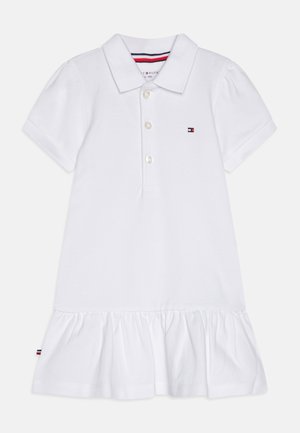 Vestido tipo polo blanco con cuello, tres botones y mangas cortas abullonadas. El dobladillo presenta un diseño con volantes y un detalle de logotipo.