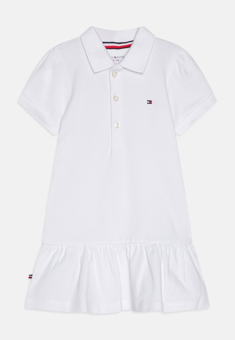 Biała sukienka polo z kołnierzykiem, trzema guzikami i krótkimi bufkami. Brzeg sukienki ozdobiony jest falbaną i detalem z logo.