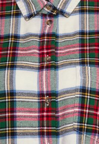Camicia a quadri con un mix di motivi a scacchi rossi, verdi, blu e gialli, con chiusura frontale a bottoni e una piccola tasca sul petto.