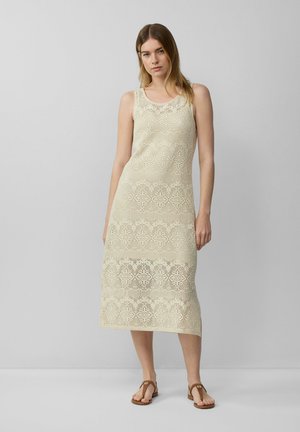 Knee-length, sleeveless dress in light beige crochet with floral patterns and open-knit texture; paired with flat, brown sandals.