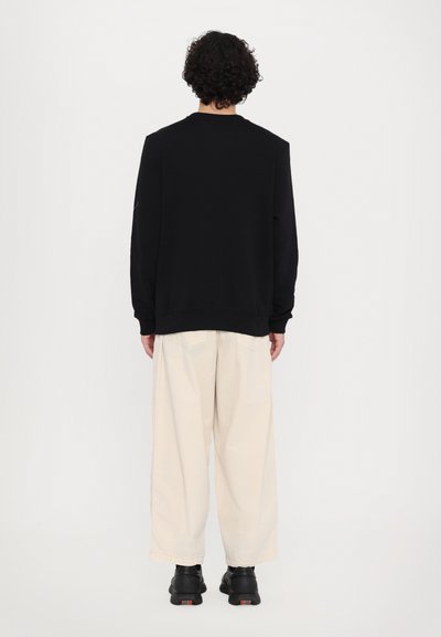 Sort sweatshirt med lange ærmer, ribbede manchetter og rund halsudskæring, parret med løse cremede bukser og sorte sneakers.