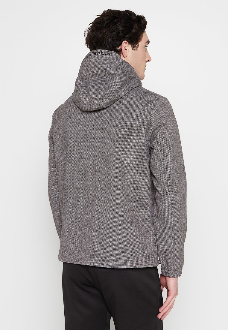 Grijze textuurjasje met een capuchon, met een subtiel patroon en een logo-accent op de achterkant. Lange mouwen en een relaxte pasvorm.