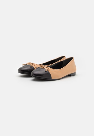 Ballerines en cuir tan et noir avec un bout arrondi, présentant un embout noir, un détail de nœud décoratif et un petit talon.