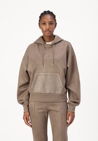 Sudadera con capucha de gran tamaño en color beige, con un bolsillo frontal, dobladillo acanalado y cordón ajustable. Está hecha de un tejido texturizado con un ligero brillo.