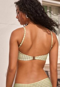 Zöld és fehér kockás bikini felső állítható pántokkal és aranyszínű csattal a hátsó részen. Sima textúra, minimalista dizájn.