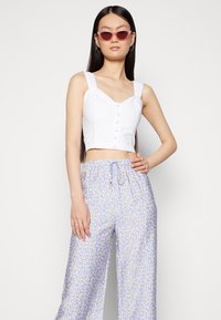 Top branco cortado com botões e alças largas, combinado com calças soltas de padrão floral em azul claro, com uma cintura elástica.