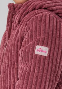 Rosa strukturierte Kapuzenjacke mit vertikalen Streifen, ausgestattet mit einem auffälligenLogo-Patch am Ärmel und geripptem Material für Wärme.