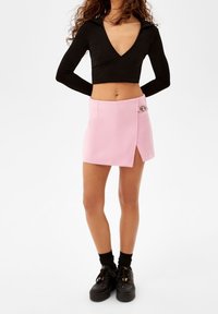 Black long-sleeve cropped top with a V-neck and wrap design, paired with a pink mini skirt featuring a side slit and decorative hardware.