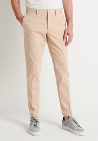 Beige skräddarsydda byxor i lätt tyg med slät front, sidofickor och smal passform, kombinerade med grå sneakers.