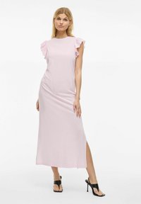 Różowa sukienka maxi z falbaniastymi krótkimi rękawami, miękką teksturą, lekkim rozcięciem po bokach i prostym okrągłym dekoltem, zestawiona z czarnymi sandałami na obcasie.