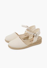 Beige canvas espadrilles met verstelbare enkelband, jute-omhulde wigzool, ronde neus en een minimalistisch design.