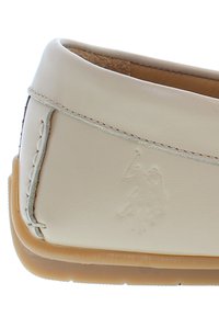 Close-up of beige leather loafer with visible stitching and embossed polo player logo above light brown rubber sole.