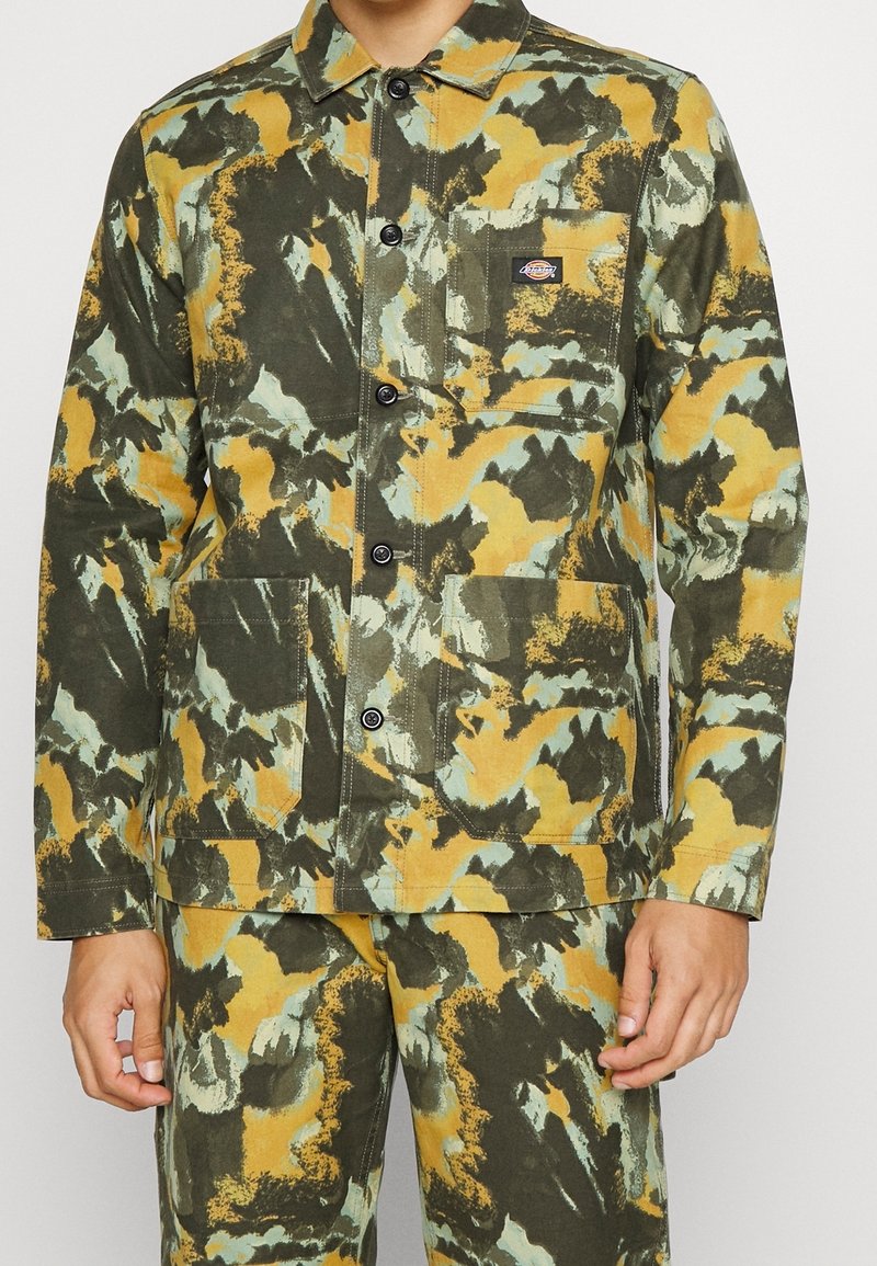 Grön-och-gul mönstrad jacka i canvas med knappstängning framtill, krage och två framfickor. Har en logotyp-patch på vänster bröst.