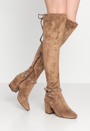 Brązowe zamszowe kozaki do kolan na klockowym obcasie, z bocznymi zamkami oraz ozdobnymi paskami zdobionymi wielobarwnymi kamieniami szlachetnymi.