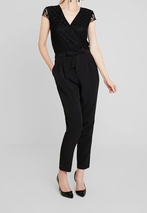 Czarny kombinezon o kroju kopertowym z krótkimi rękawami, z fakturowanym wzorem w kropki na górnej części oraz wiązanym paskiem w talii.
