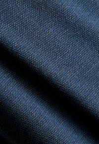 Marineblaues gewebtes Material mit feiner struktureller Musterung. Der Stoff wirkt weich und strapazierfähig und zeigt leichte Variationen in der Farbtiefe.