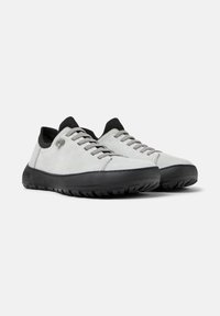 Scarpe da ginnastica grigio chiaro in suede, con suole in gomma nera, lacci grigi e un design a profilo basso. Superficie testurizzata con dettagli minimalisti.