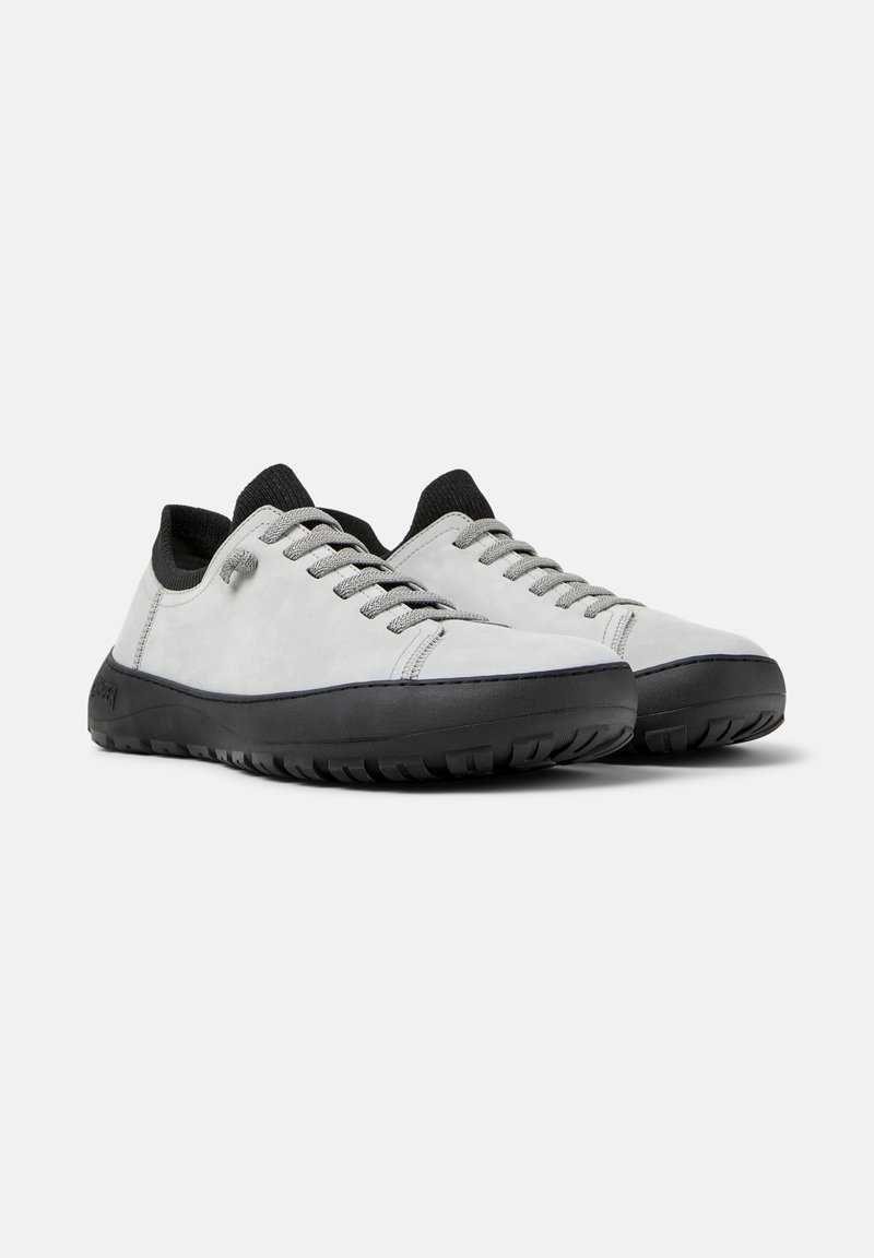 Light gray athletic shoes made of suede, featuring black rubber soles, gray laces, and a low profile design. Textured surface with minimalist detailing.
