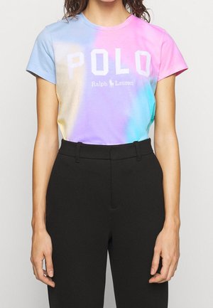Žena nosící pastelové batikované tričko Ralph Lauren Polo v růžové, modré a žluté barvě, v kombinaci s černými kalhotami s vysokým pasem.
