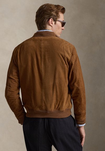 Καφέ μπουφάν bomber από σουέντ με ριμπ μανσέτες και πάτο· διαθέτει μινιμαλιστικό σχέδιο και λείο υλικό, σε άποψη από πίσω.