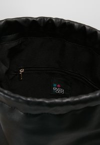 Vue intérieure d'un sac en cuir noir montrant une poche zippée et une étiquette en tissu avec des formes géométriques colorées et du texte.
