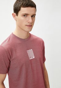 Czerwony heather t-shirt z krótkim rękawem, wykonany z miękkiego materiału, z okrągłym dekoltem, z białym nadrukiem „GOOD!” z przodu.