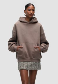 Brown oversized hoodie with front pocket, ribbed cuffs, and hem. Paired with a textured skirt featuring a herringbone pattern.