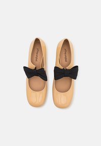 Beige patent leather flats with round toe, black fabric bows on the front, and tan insoles. Smooth texture and minimalist design.