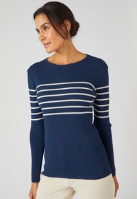 Marineblauwe geribbelde trui met witte horizontale strepen, voorzien van een ronde halslijn en lange mouwen. De pasvorm lijkt iets getailleerd.
