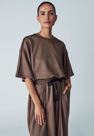 Brown, oversized top with short sleeves, made from smooth fabric. Drawstring waistband on matching relaxed-fit pants, featuring side pockets.