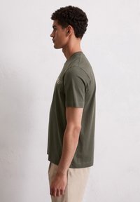 Groene katoenen t-shirt met korte mouwen en een ronde hals, voorzien van een subtiele logo in een lichtere tint aan de voorkant, gecombineerd met lichte broek.