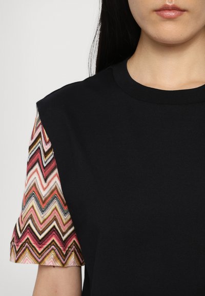 Μαύρη βαμβακερή μπλούζα με κοντά μανίκια, με ζιγκ-ζαγκ σχέδιο σε ροζ, κρέμ και καφέ αποχρώσεις στα μανίκια.