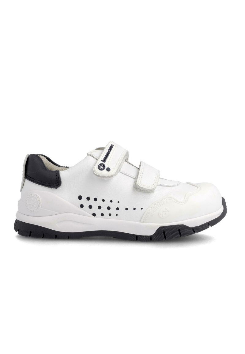 Zapato de cuero blanco con acentos negros, dos correas de Velcro, diseño perforado en el costado, suela de goma con dibujo estampado.