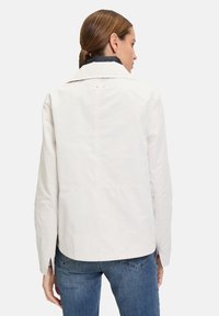 White, lightweight jacket with a large collar, back buttons, and seam detailing; paired with blue denim jeans. Smooth fabric texture.