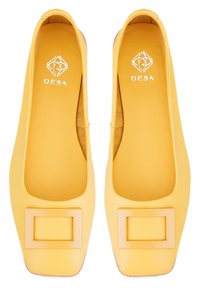 Gelbe Ballerinas mit quadratischem Zehenentwurf, weichem Ledertextur und einem auffälligen rechteckigen Akzent auf dem Blatt. Logo innen sichtbar.