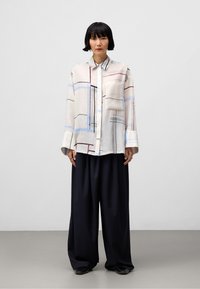 Camicia leggera a maniche lunghe con bottoni, caratterizzata da un motivo astratto in colori chiari, con una tasca sul petto e una vestibilità comoda. Pantaloni a gamba larga scuri.