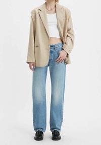 Blazer de cuadros beige con corte relajado, top corto blanco, jeans rectos de mezclilla azul claro y zapatos negros.