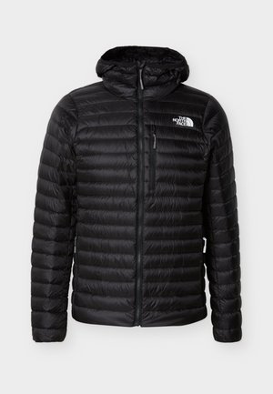 Melna dūraiņota jaka ar kapuci, priekšpuses rāvējslēdzēju un krūšu kabatu, uz kreisā krūšu vietas redzams The North Face logotips.