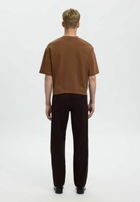 Bruine T-shirt met korte mouwen en een ronde hals, gecombineerd met zwarte rechte broek. Soepele stof en een relaxte pasvorm.